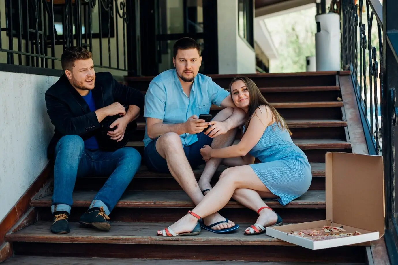 Ein Paar sitzt mit einem Freund auf den Stufen eines Hauses.